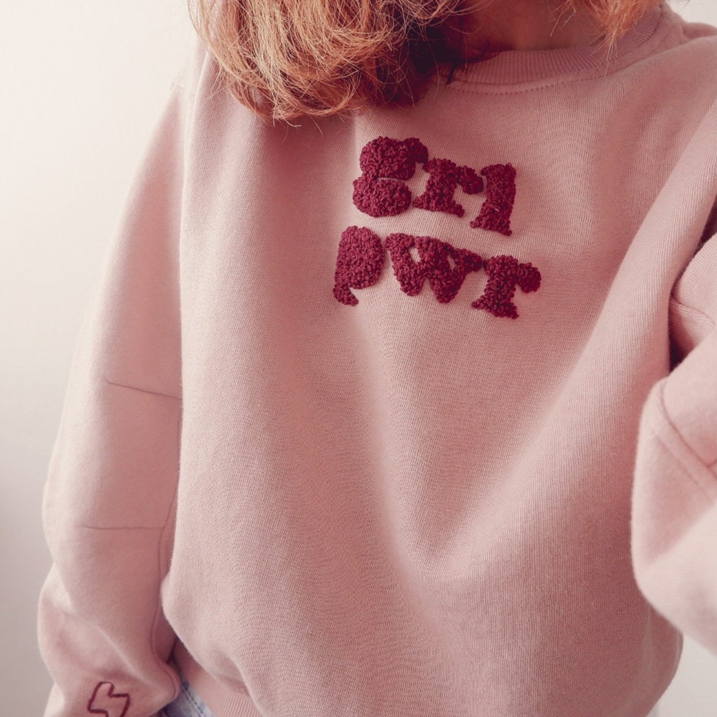 Pink sweatshirt with red text on a plain background