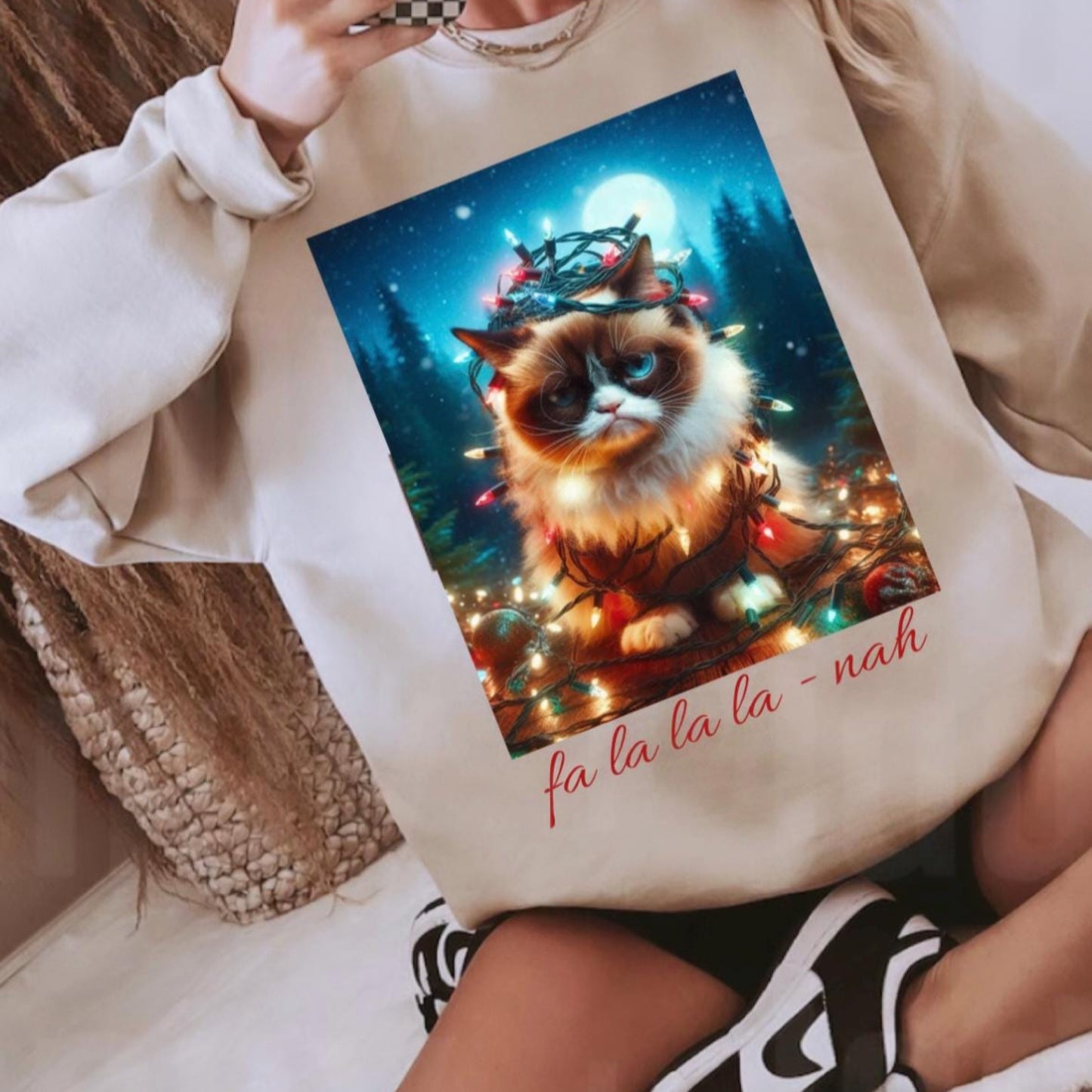 Person wearing a beige sweatshirt with a Christmas-themed cat design and 'fa la la la nah' text.