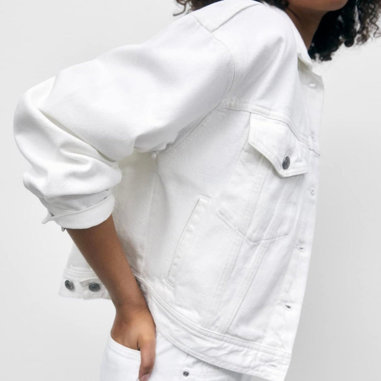 Person wearing a white denim jacket and shorts on a plain background