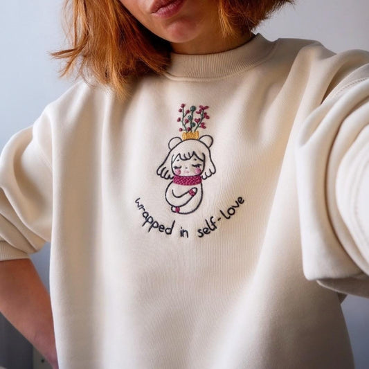 White sweatshirt with embroidered design and text on a plain background