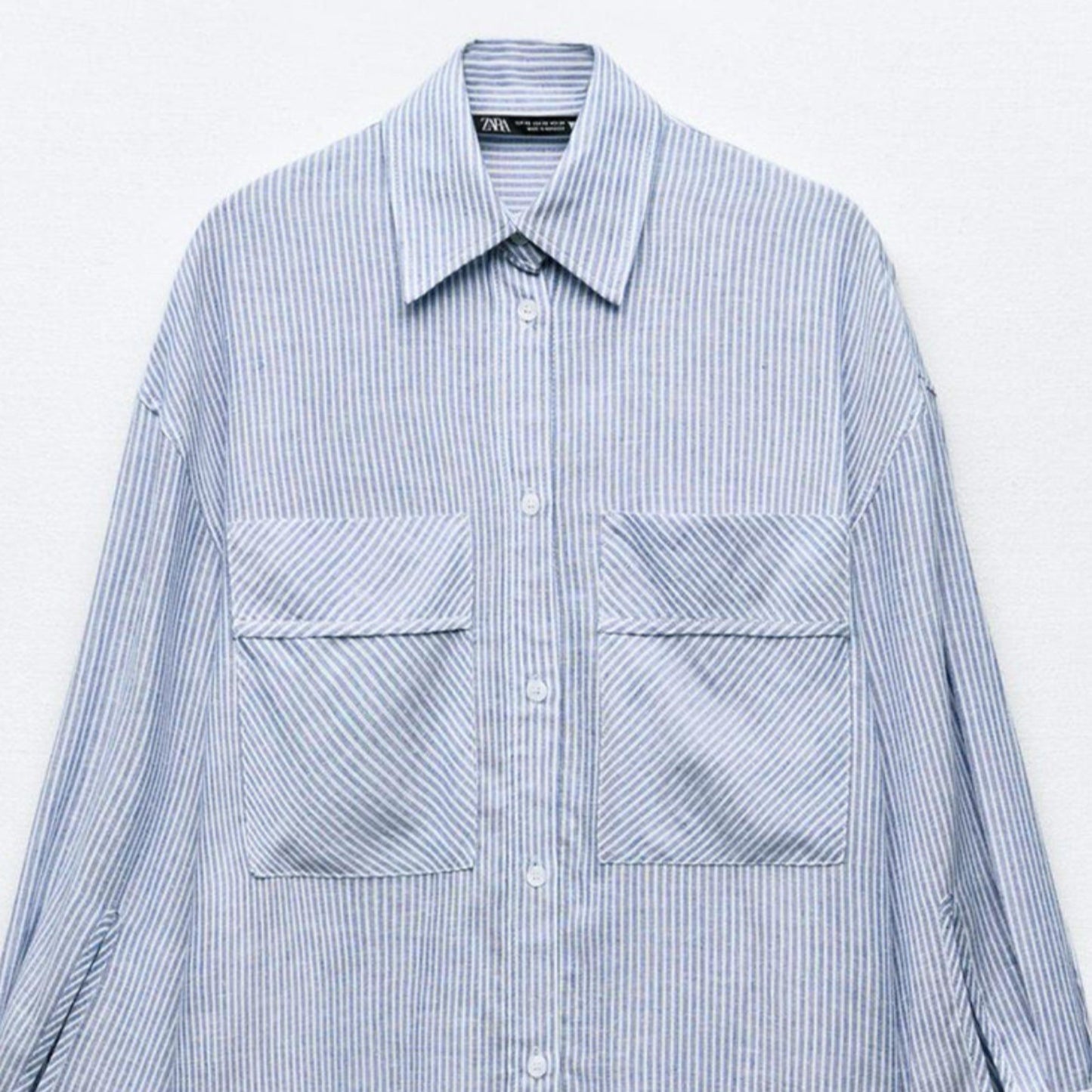 Blue and white striped shirt with two front pockets on a light gray background
