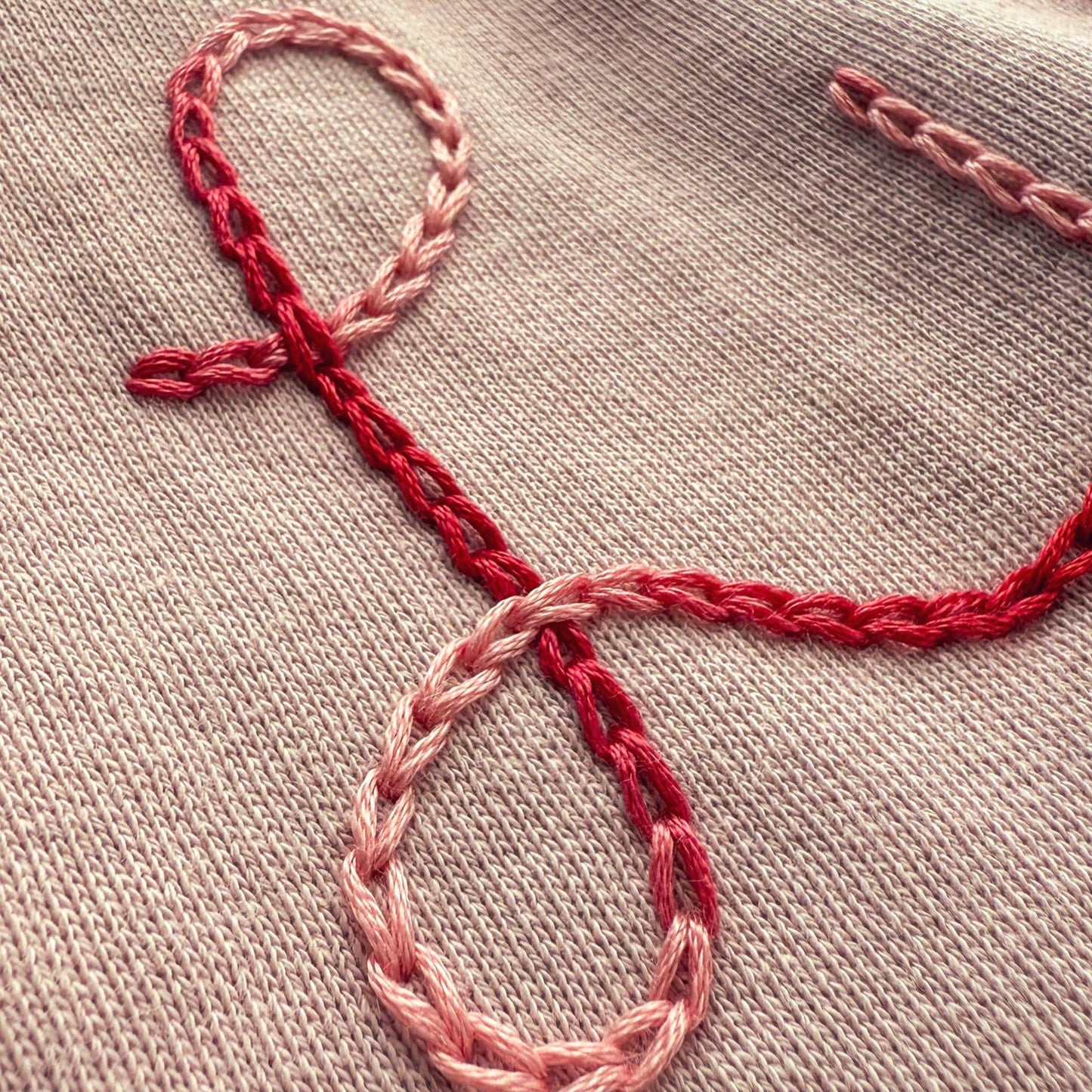 Embroidered design on a light pink sweater with red thread