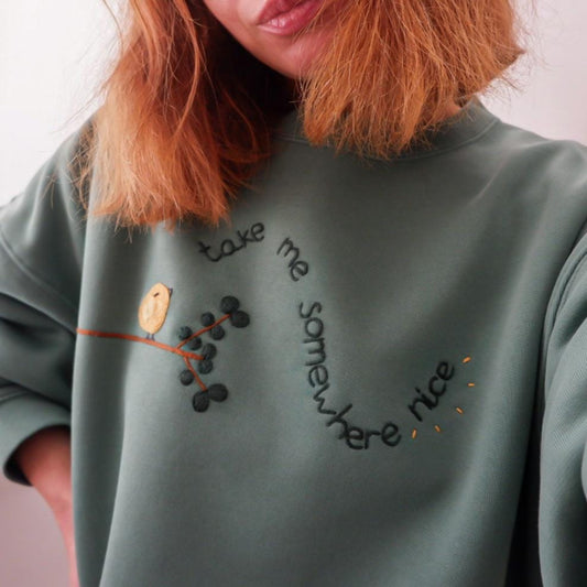 Person wearing a green sweatshirt with embroidered text and design