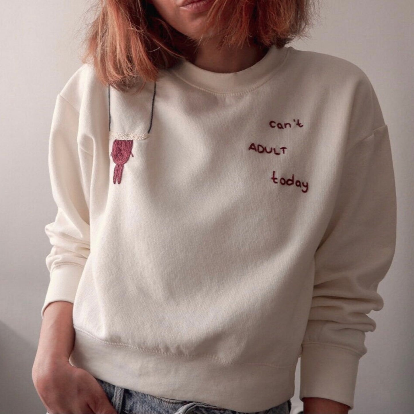 Person wearing a beige sweatshirt with text and a small graphic on a plain background