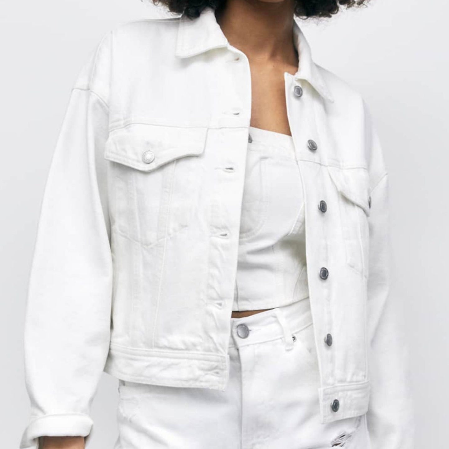Person wearing a white denim jacket and shorts on a plain background