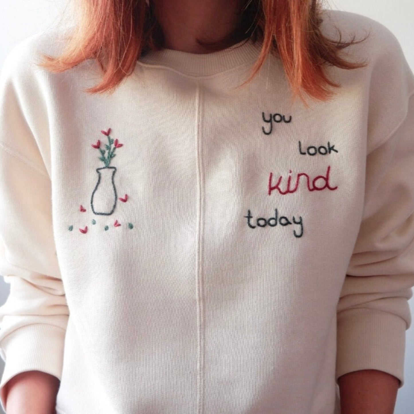 White sweatshirt with embroidered text and design on a plain background