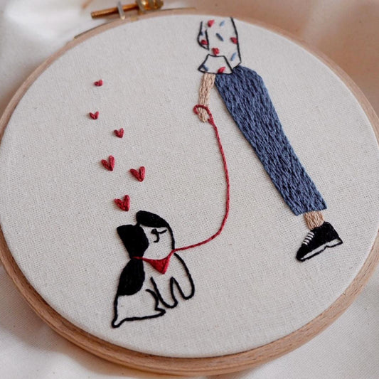 Embroidery hoop with a person walking a dog and hearts, on a light background