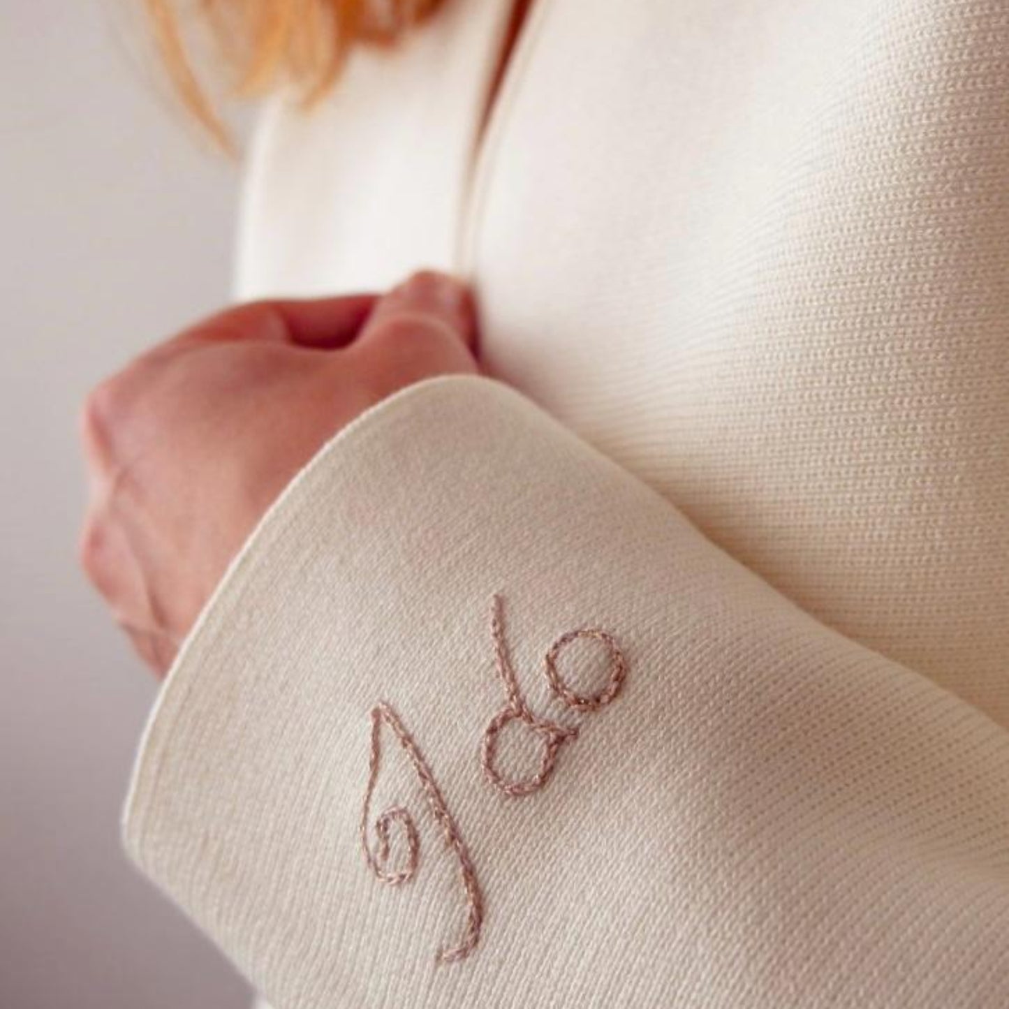 Close-up of a white garment with embroidered initials on a plain background