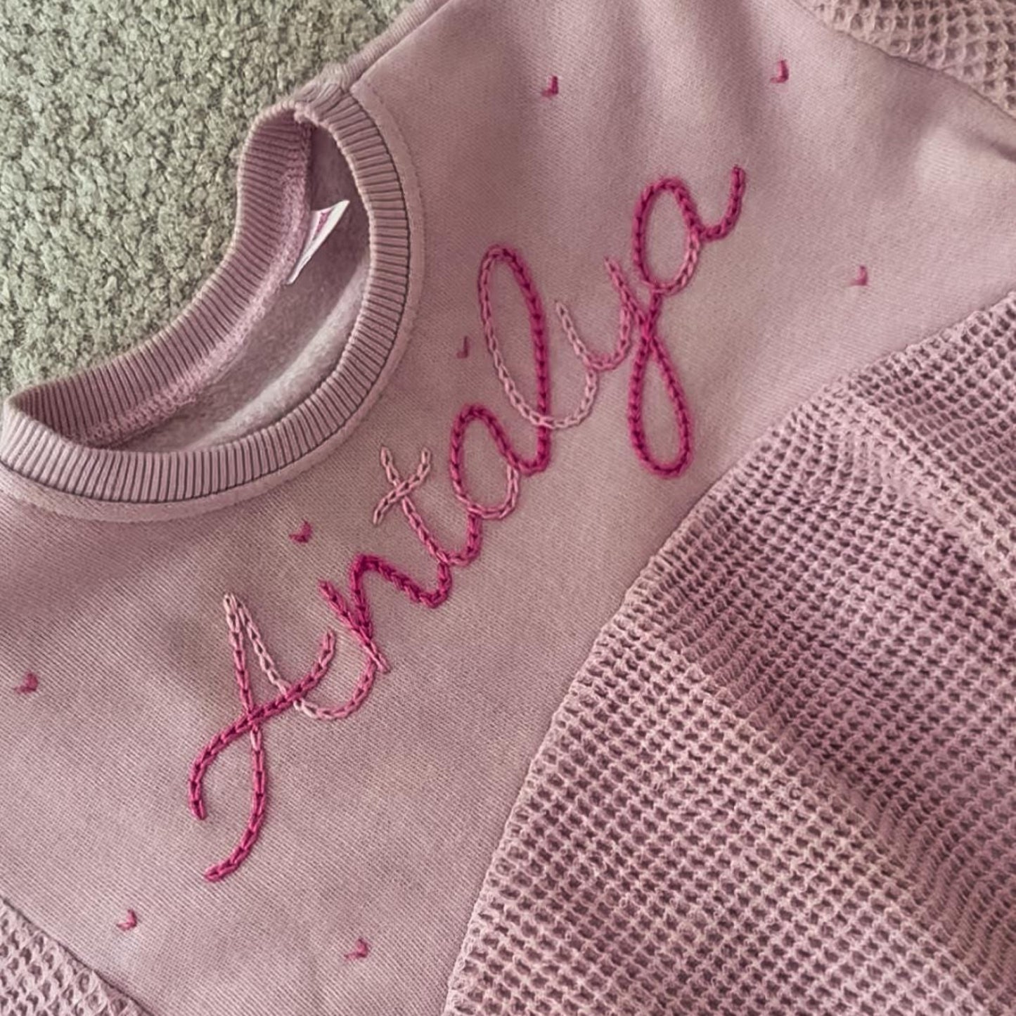Pink textured garment with embroidered name on a green surface