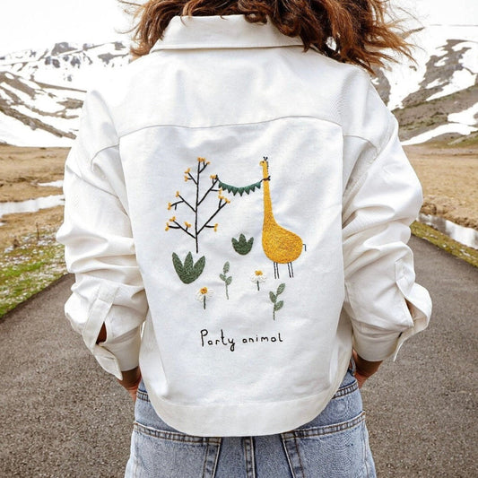 Person wearing a white jacket with a giraffe design and 'Party animal' text, standing on a road with a mountainous landscape.