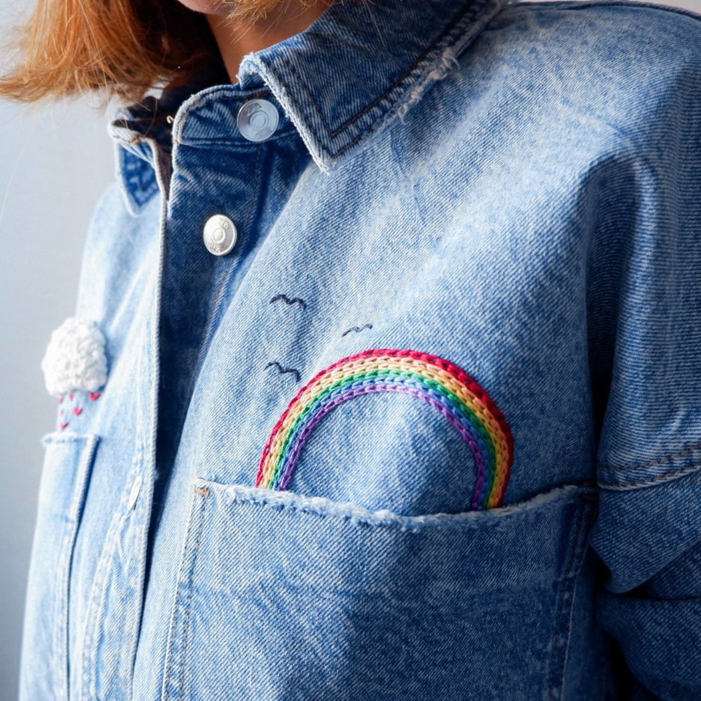 Blue denim jacket with a rainbow patch on the chest pocket against a gray background