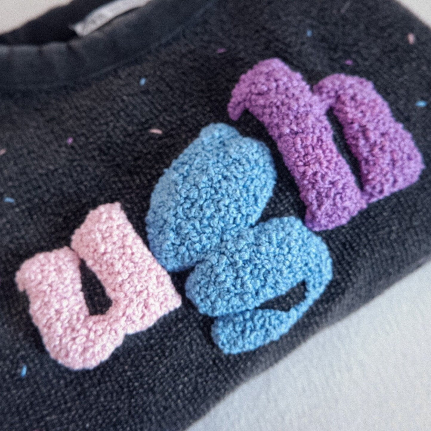 Black knitted pouch with colorful letters 'USS' on a white background
