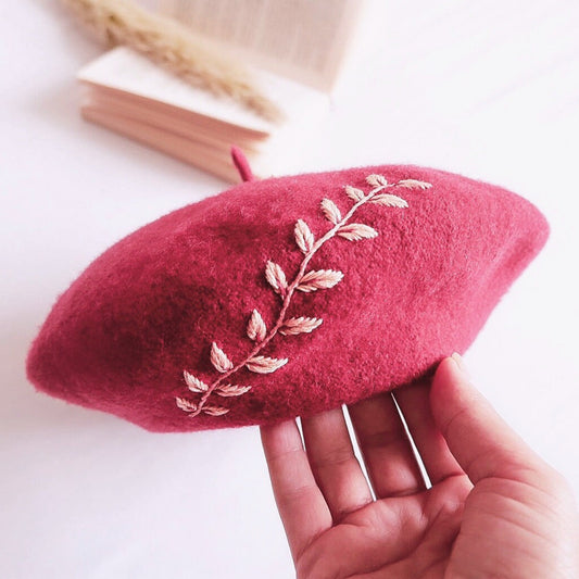 Red beret with floral embroidery held by a hand on a light background