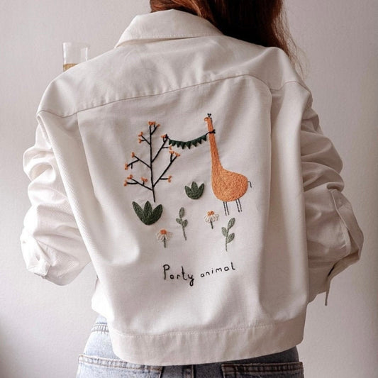 White denim jacket with giraffe and plant embroidery on a plain background