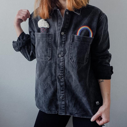 Person wearing a black denim shirt with embroidered designs on a plain background