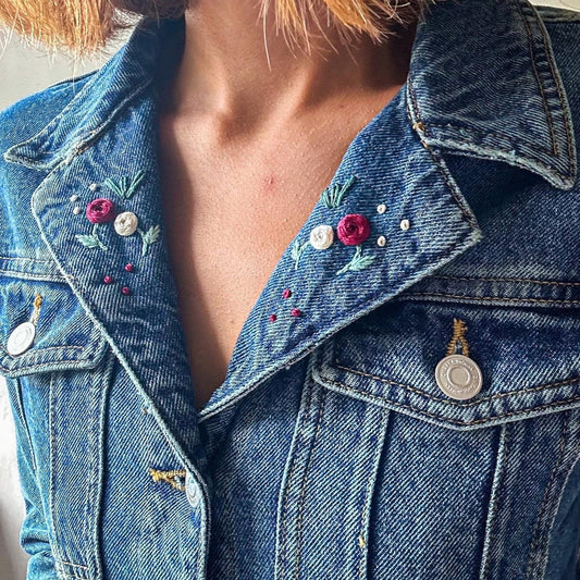 Close-up of a blue denim jacket with floral embroidery and decorative buttons.