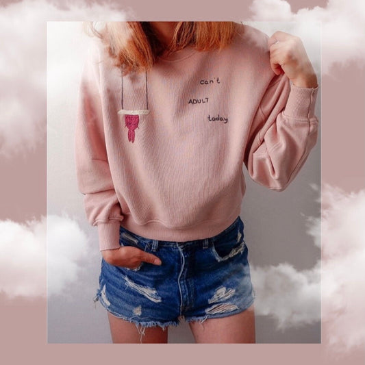 Person wearing a pink sweatshirt with text and denim shorts against a cloud-themed background