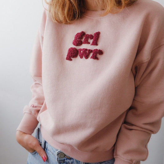 Pink sweatshirt with red text worn by a person against a plain background