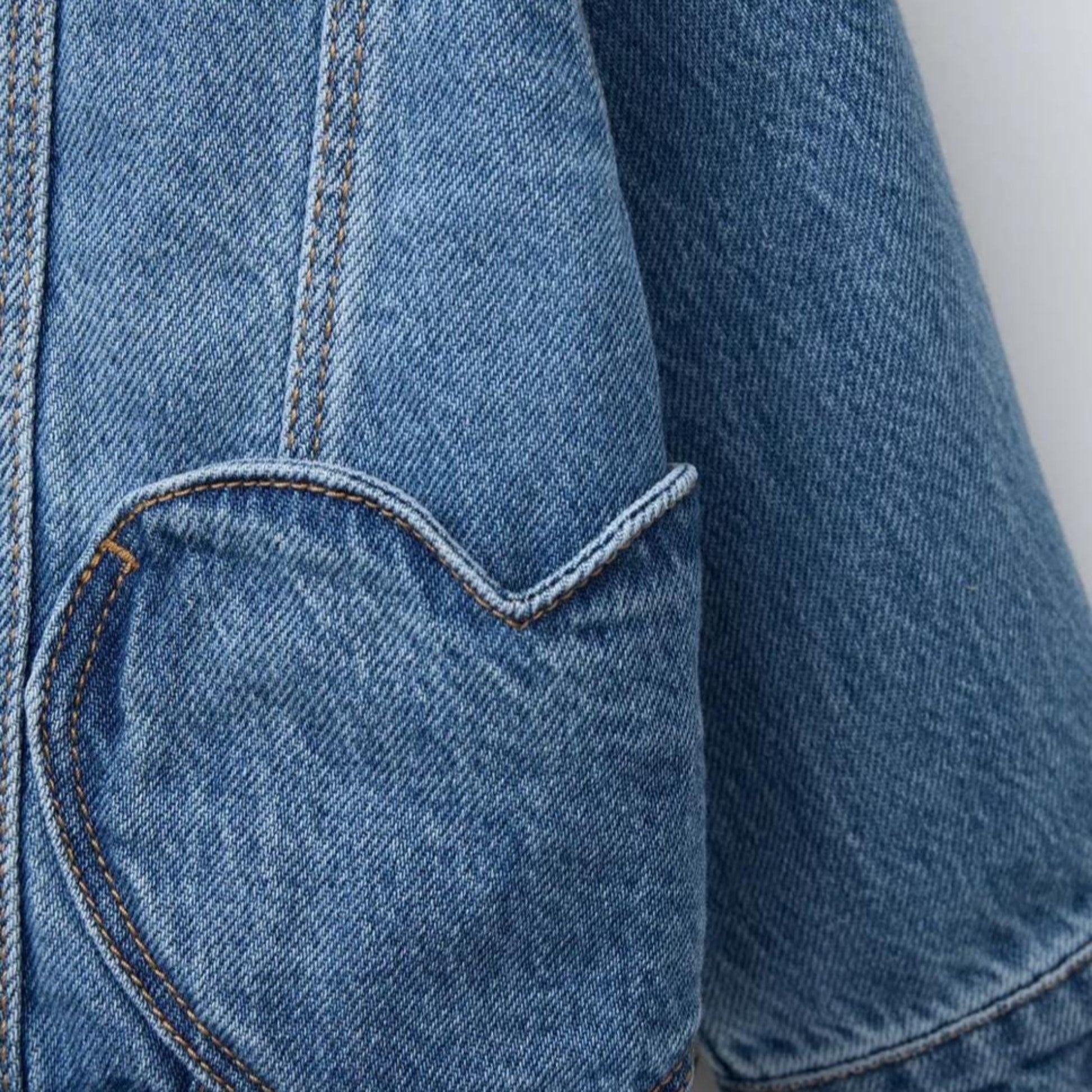Close-up of a blue denim jacket with a heart-shaped pocket on a light gray background