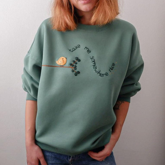 Person wearing a green sweatshirt with a bird and branch design on a plain background