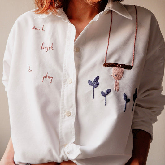 White shirt with embroidered text and design on a neutral background