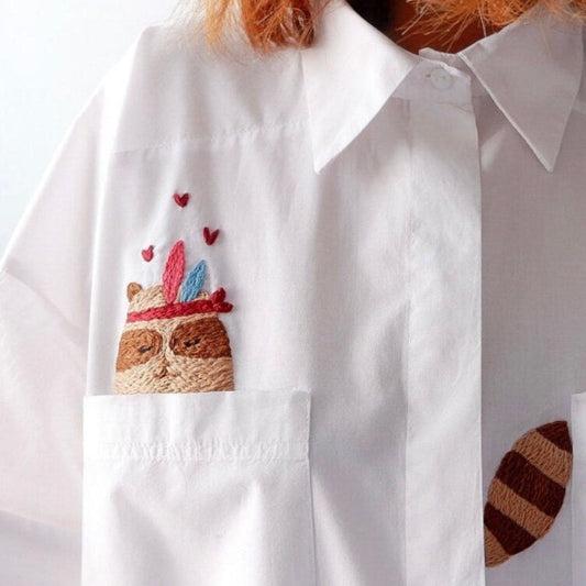 White shirt with embroidered racoon design on a white background