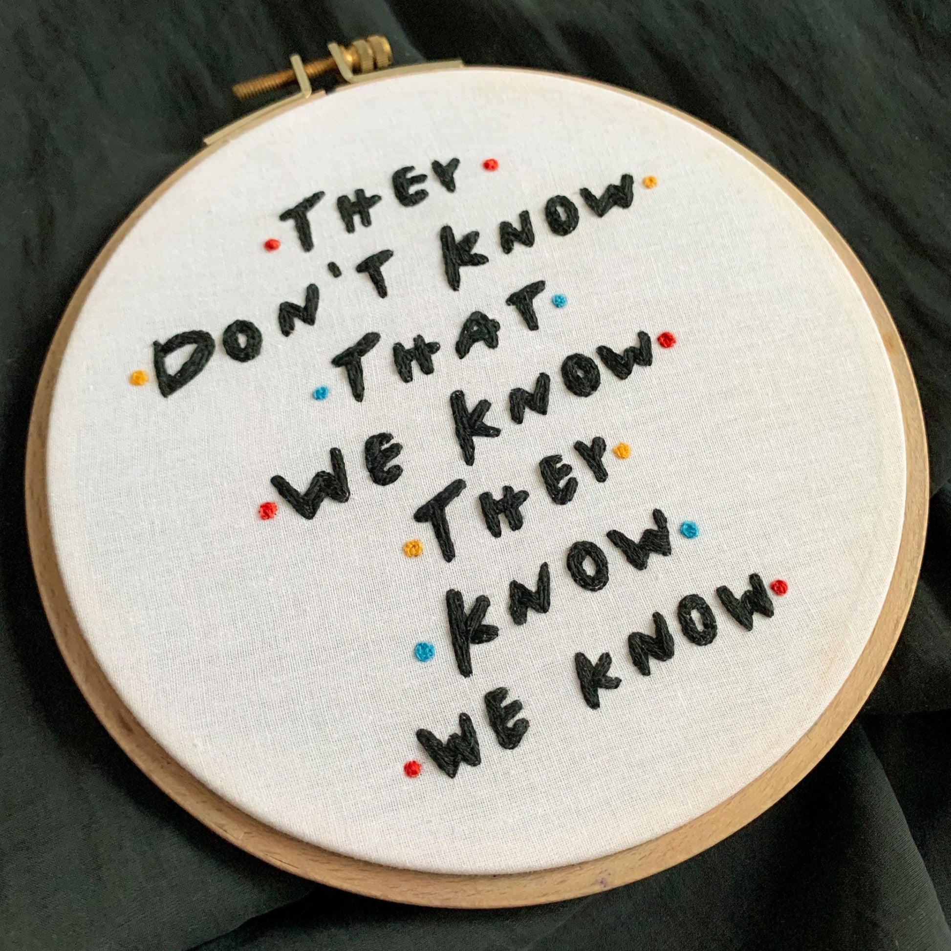 Embroidery hoop with text 'They don't know that we know they know we know' on a dark fabric background