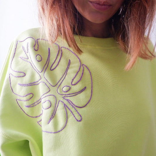 A close-up image of a neon green sweatshirt with a hand embroidered monstera leaf design on the front.