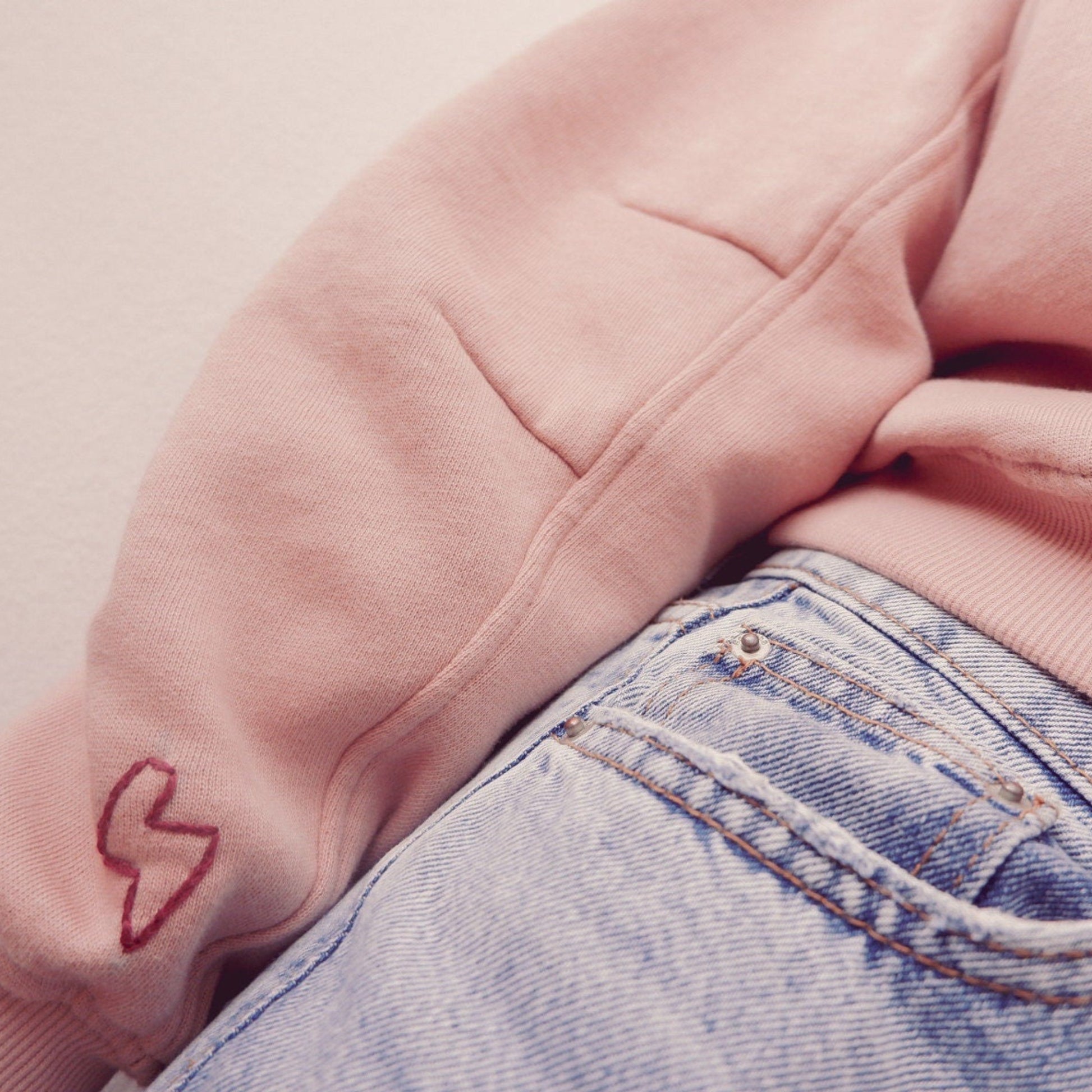 Pink hoodie with a red heart design on sleeve and blue jeans.