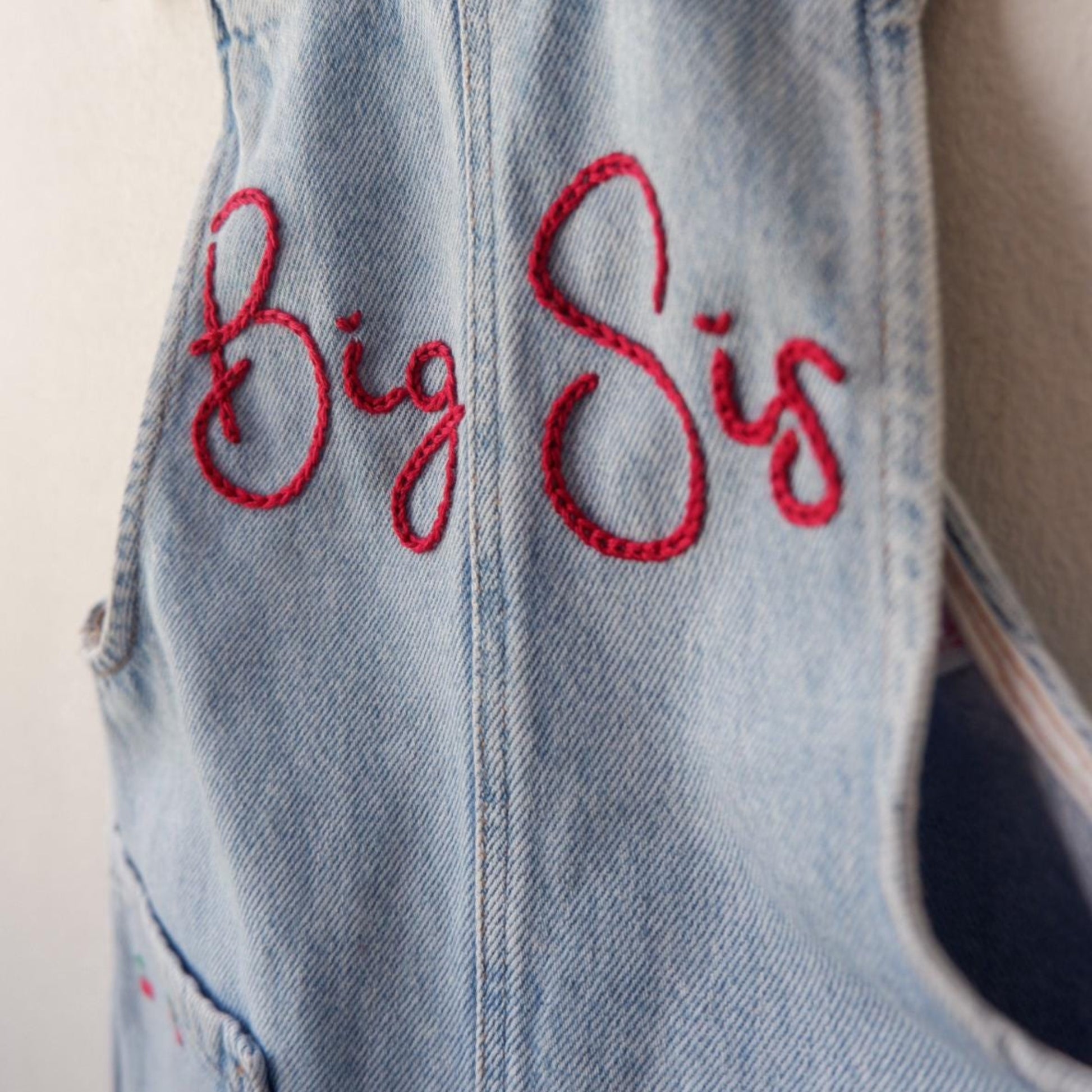 Denim overalls with 'Big Sis' embroidered in red on a plain background