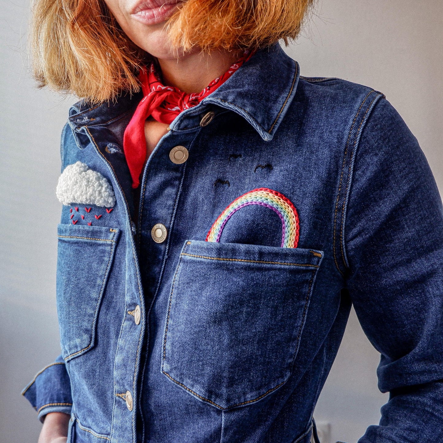 A person wearing a denim jacket with a hand-embroidered rain and rainbow motif on it.