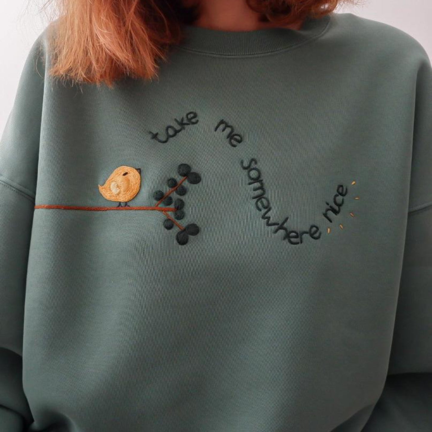 Green sweatshirt with embroidered design of a bird and text on a plain background