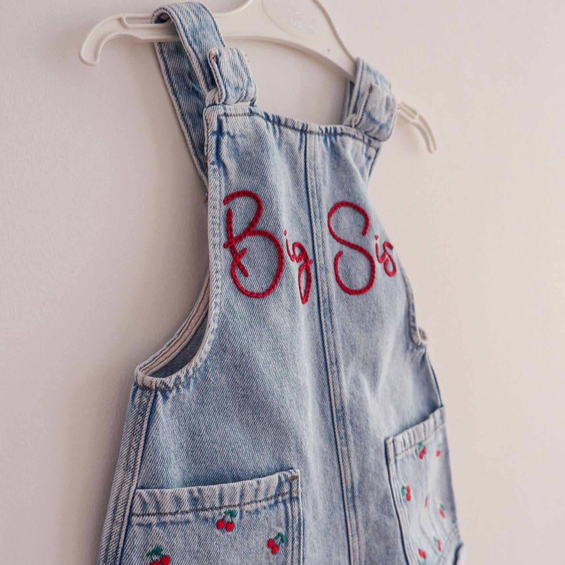 Denim overall dress with red embroidery on a white background