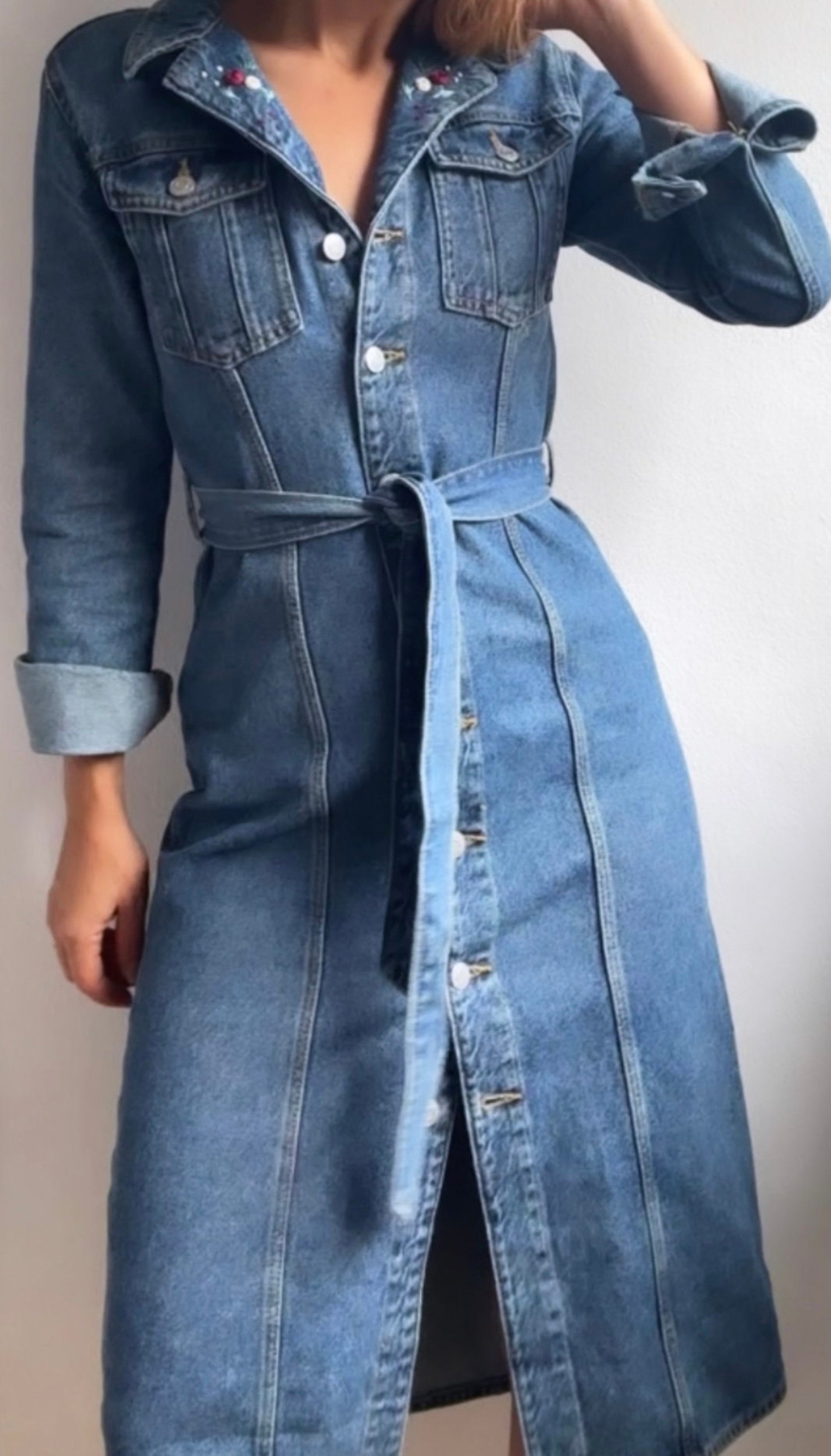 Long denim coat worn by a person on a plain background