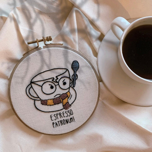 Hand embroidery hoop art depicting a coffee cup with the text 'ESPRESSO PATRONUM' on a wall, next to a cup of coffee.