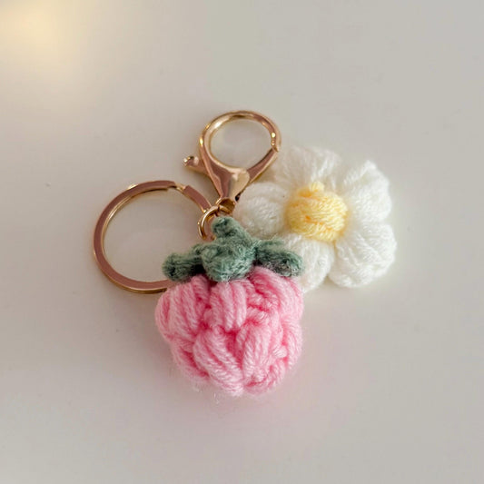 Crocheted pink strawberry keychain with a white flower on a light gray background