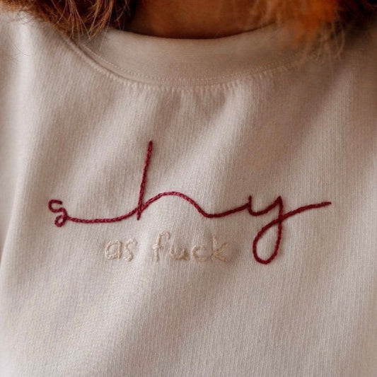 Textured fabric with embroidered text 'shy as fuck' on a beige background