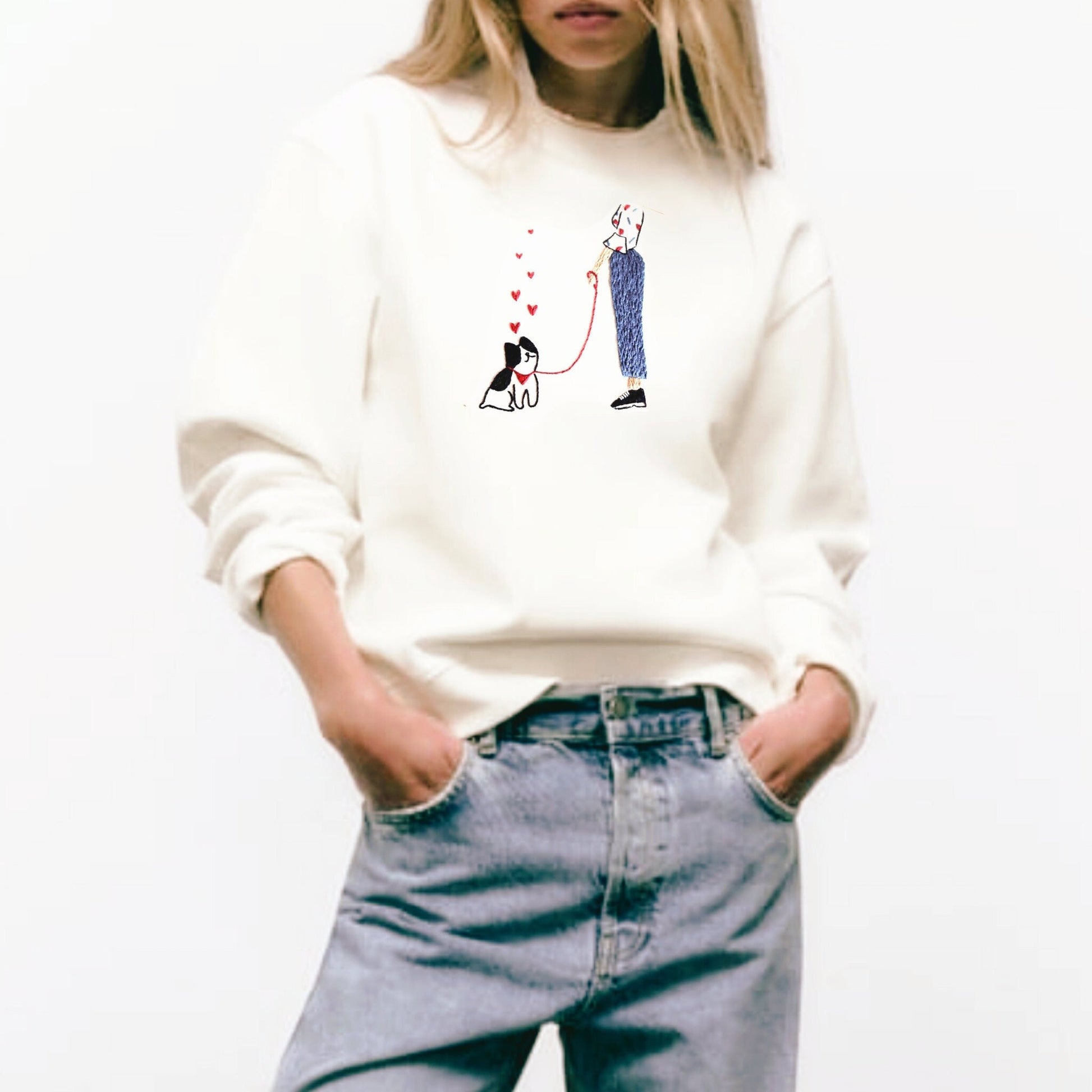 Person wearing a white sweatshirt with a graphic design and blue jeans on a white background