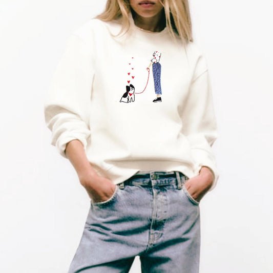 Person wearing a white sweatshirt with a graphic design and blue jeans on a white background