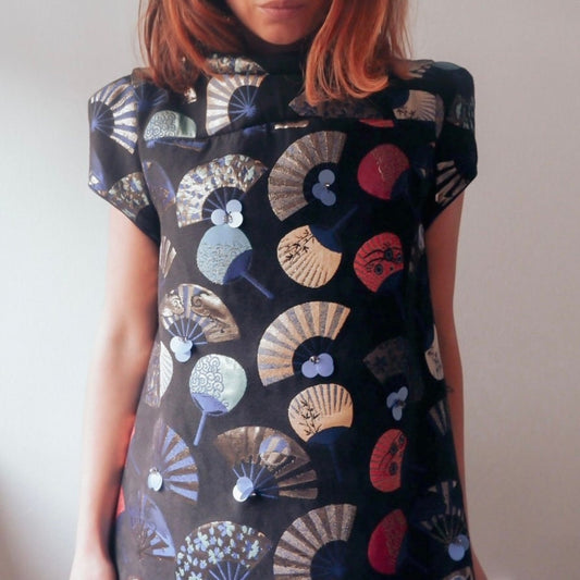 Person wearing a black dress with colorful fan pattern against a plain background