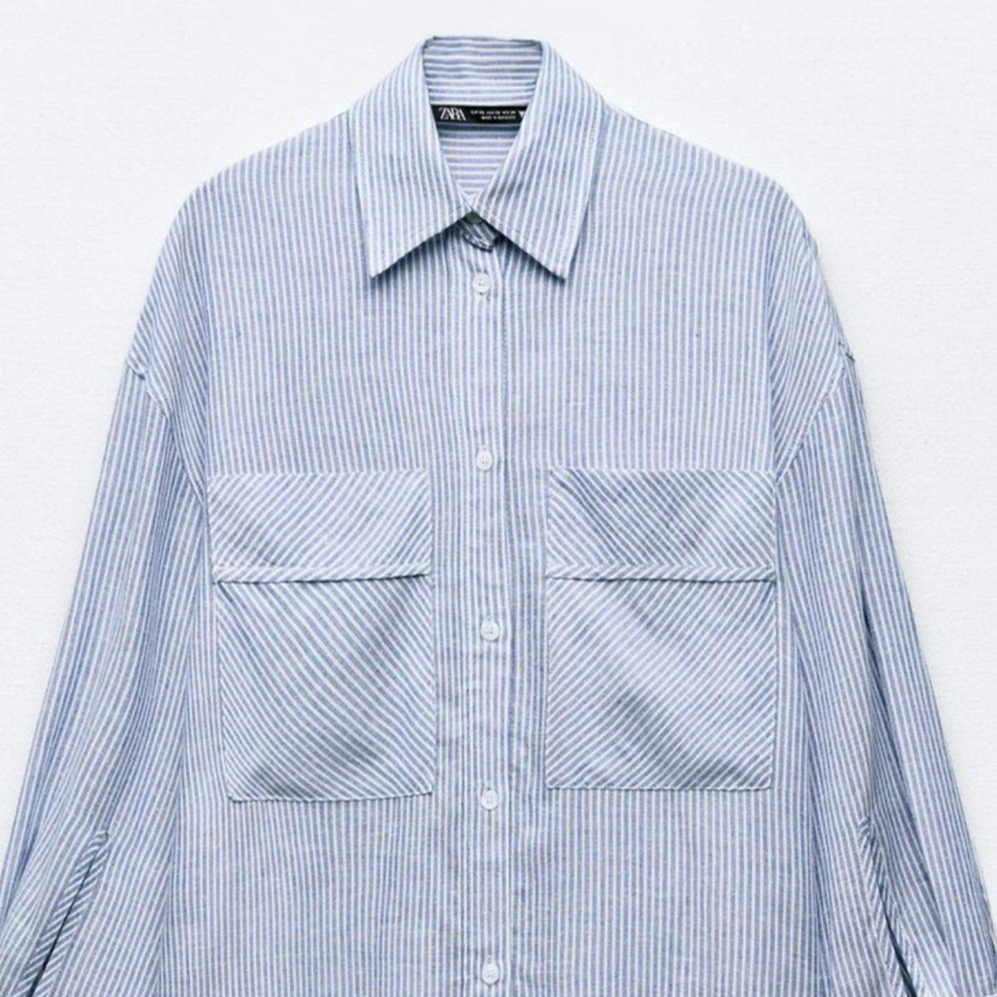 Blue and white striped shirt with two front pockets on a light gray background