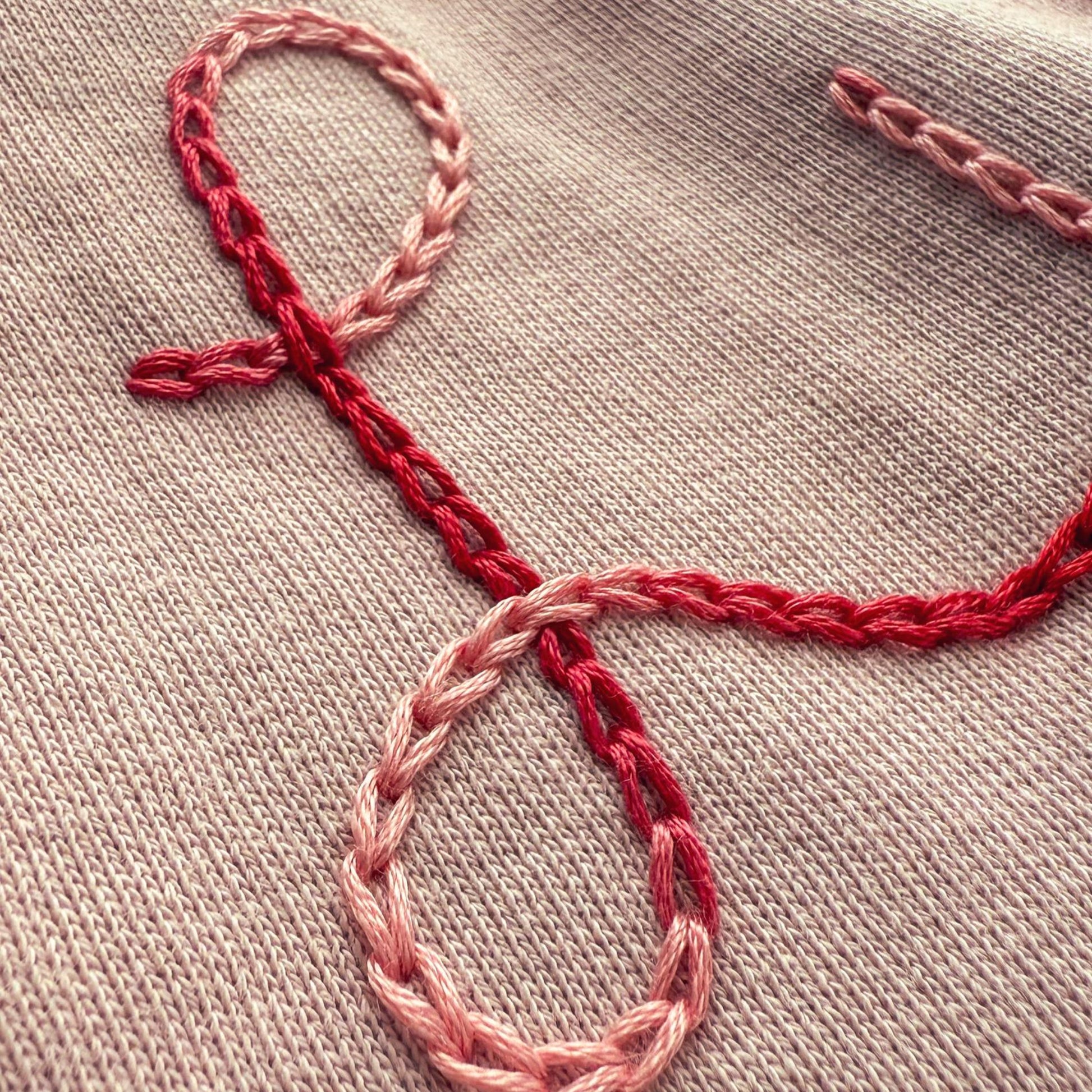 Embroidered design on a light pink sweater with red thread