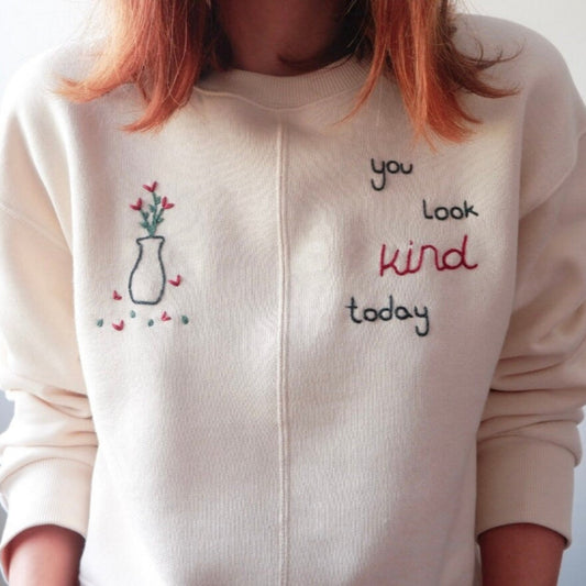 White sweatshirt with embroidered text and design on a plain background