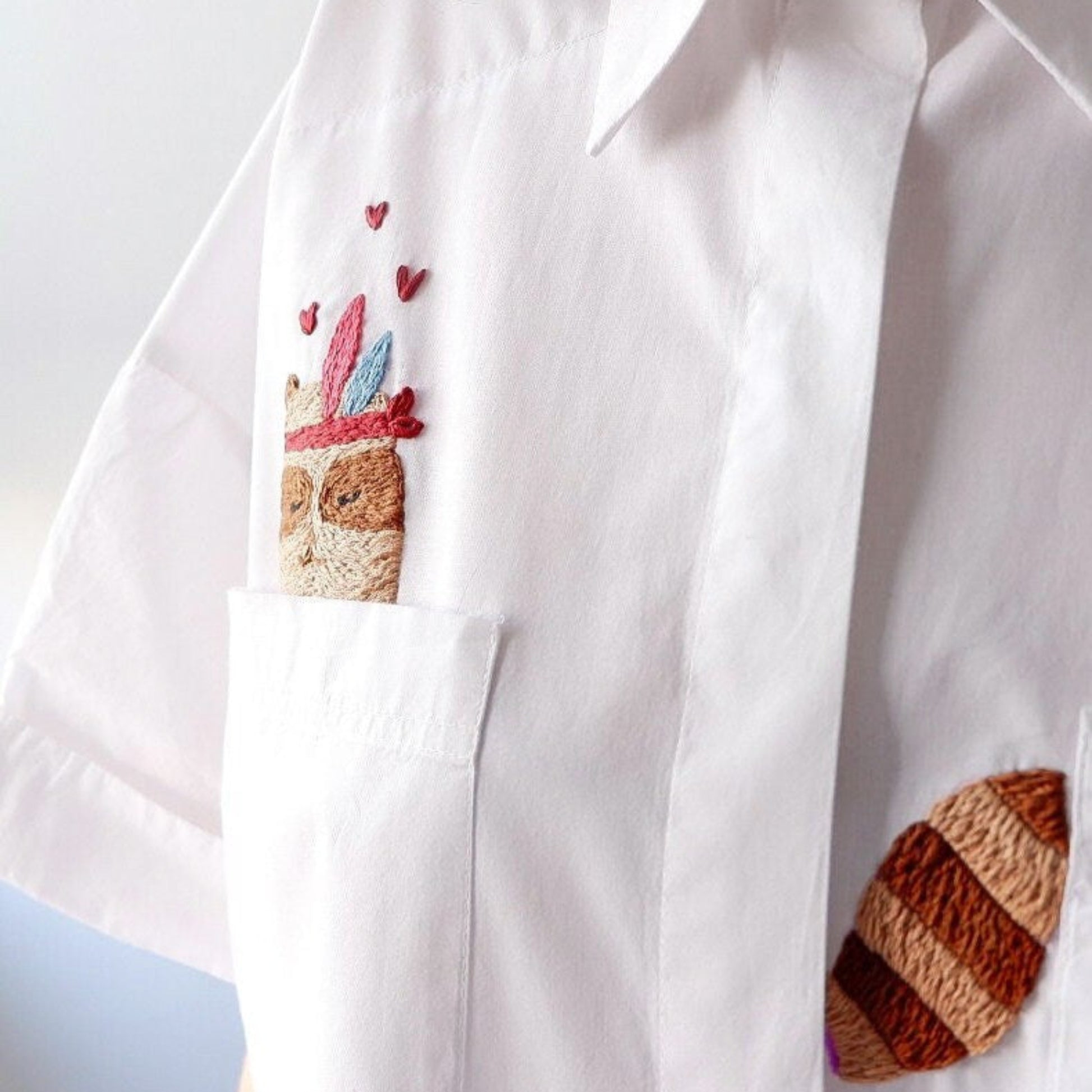 White shirt with embroidered racoon designs on a plain background