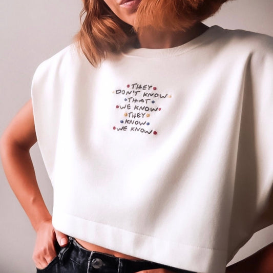 White sleeveless top with embroidered text worn by a person against a neutral background