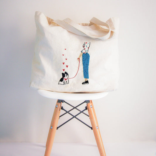 Tote bag with a design of a person walking a dog on a chair against a white background